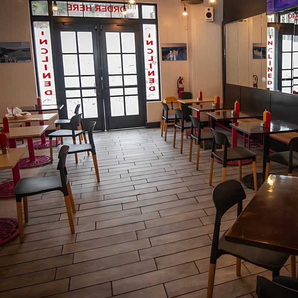 Interior of Inclined Burgers and Brews, showing empty tables, chairs, and a bright entrance.