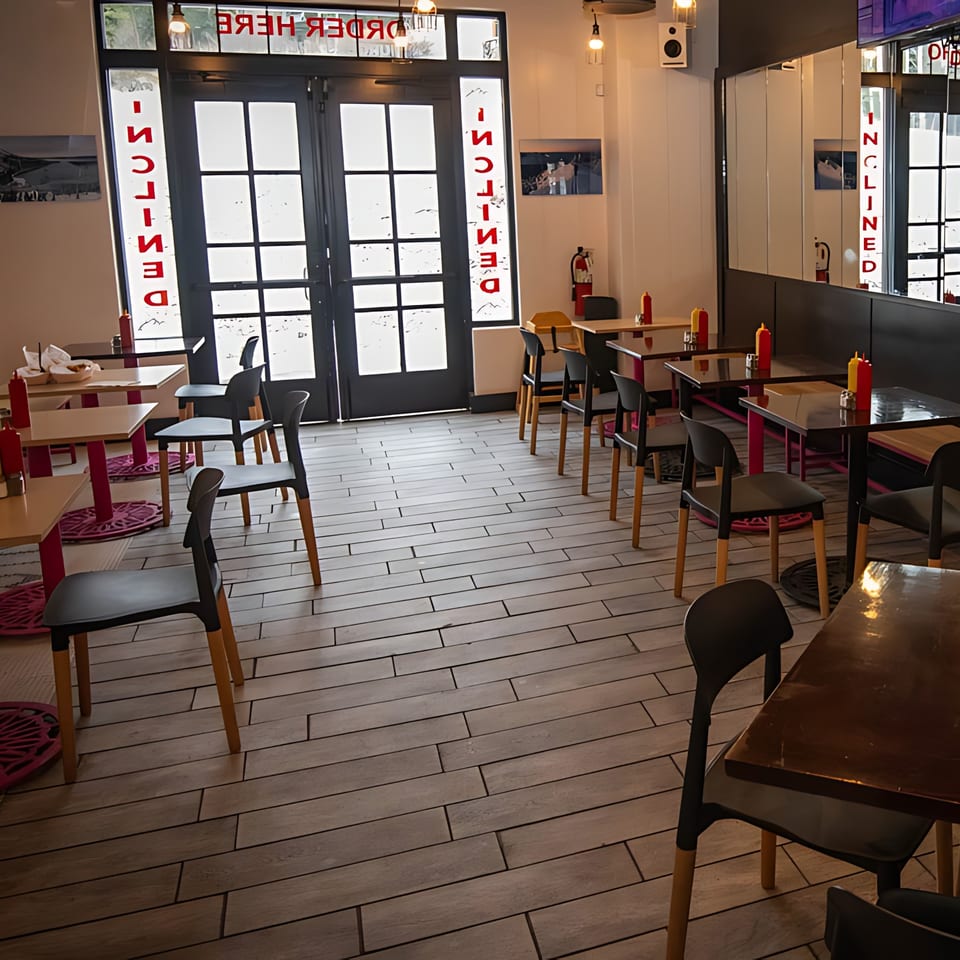 Interior of Inclined Burgers and Brews, showing empty tables, chairs, and a bright entrance.