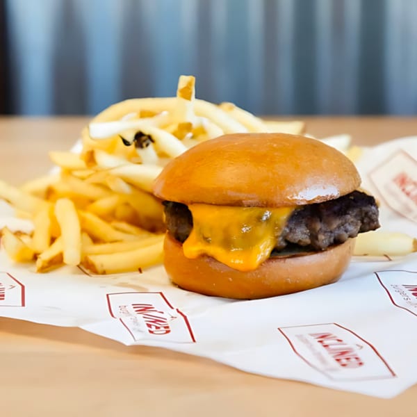 Inclined Burgers and Brews cheeseburger with melted cheese and a side of golden fries on branded paper.