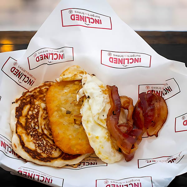 Inclined Burgers and Brews breakfast with pancakes, hash brown, fried eggs, and bacon.