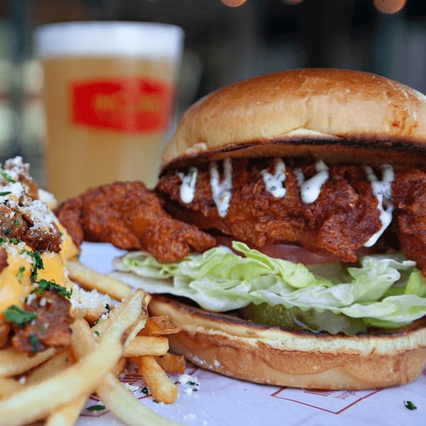 Inclined Burgers and Brews' spicy chicken sandwich with fries and a beer in the background.