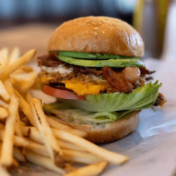 Inclined Burgers and Brews' burger with avocado, bacon, cheese, lettuce, and tomato, served with fries.