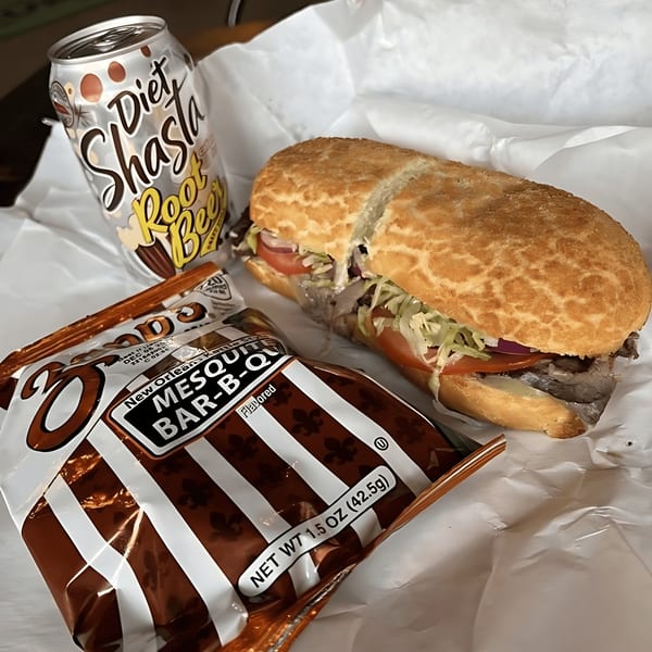 A sandwich with lettuce, tomato, and meat, next to a bag of chips and a Diet Shasta Root Beer.