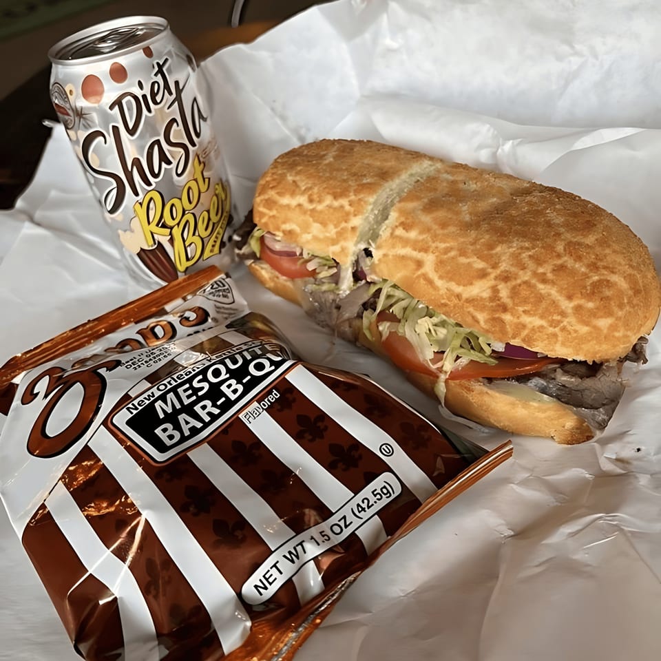 A sandwich with lettuce, tomato, and meat, next to a bag of chips and a Diet Shasta Root Beer.