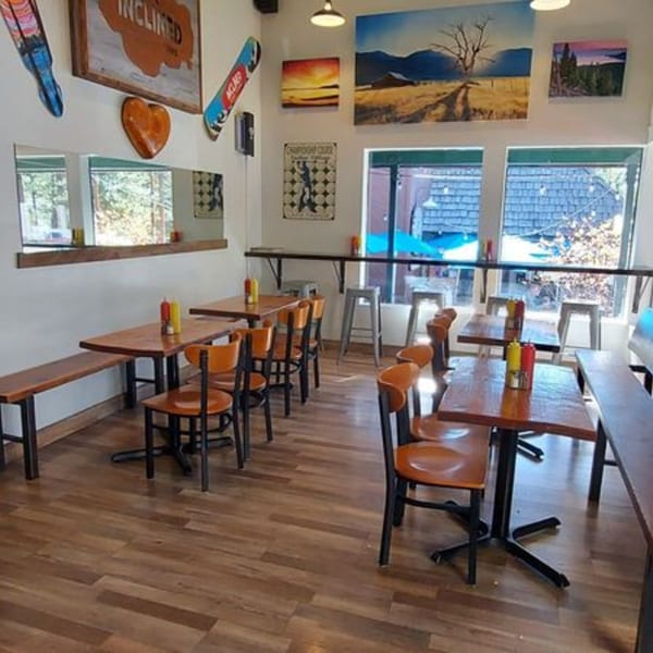 Inclined Burgers and Brews dining room with wooden tables, orange chairs, and wall art.