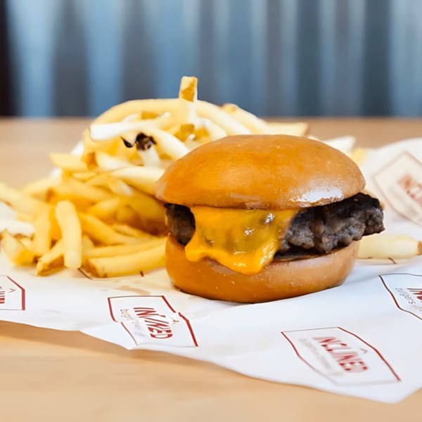 Inclined Burgers and Brews cheeseburger with melted cheese and a side of golden fries on branded paper.