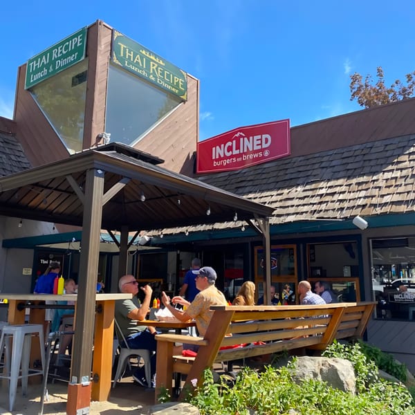 Inclined Burgers and Brews restaurant exterior with outdoor patio seating and customers under a canopy.
