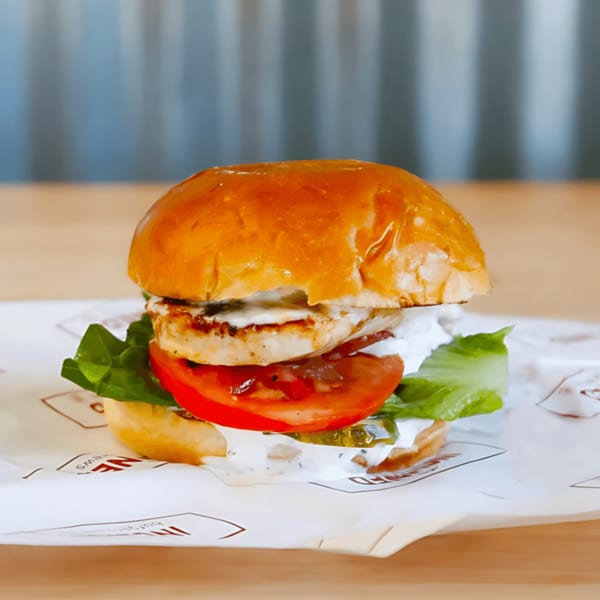 Grilled chicken burger with lettuce, tomato, pickles, and white sauce on a brioche bun.